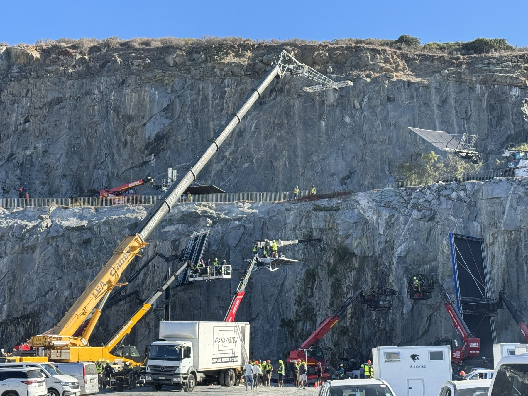 Multiple cranes and elevated work platforms supporting a film production at a quarry